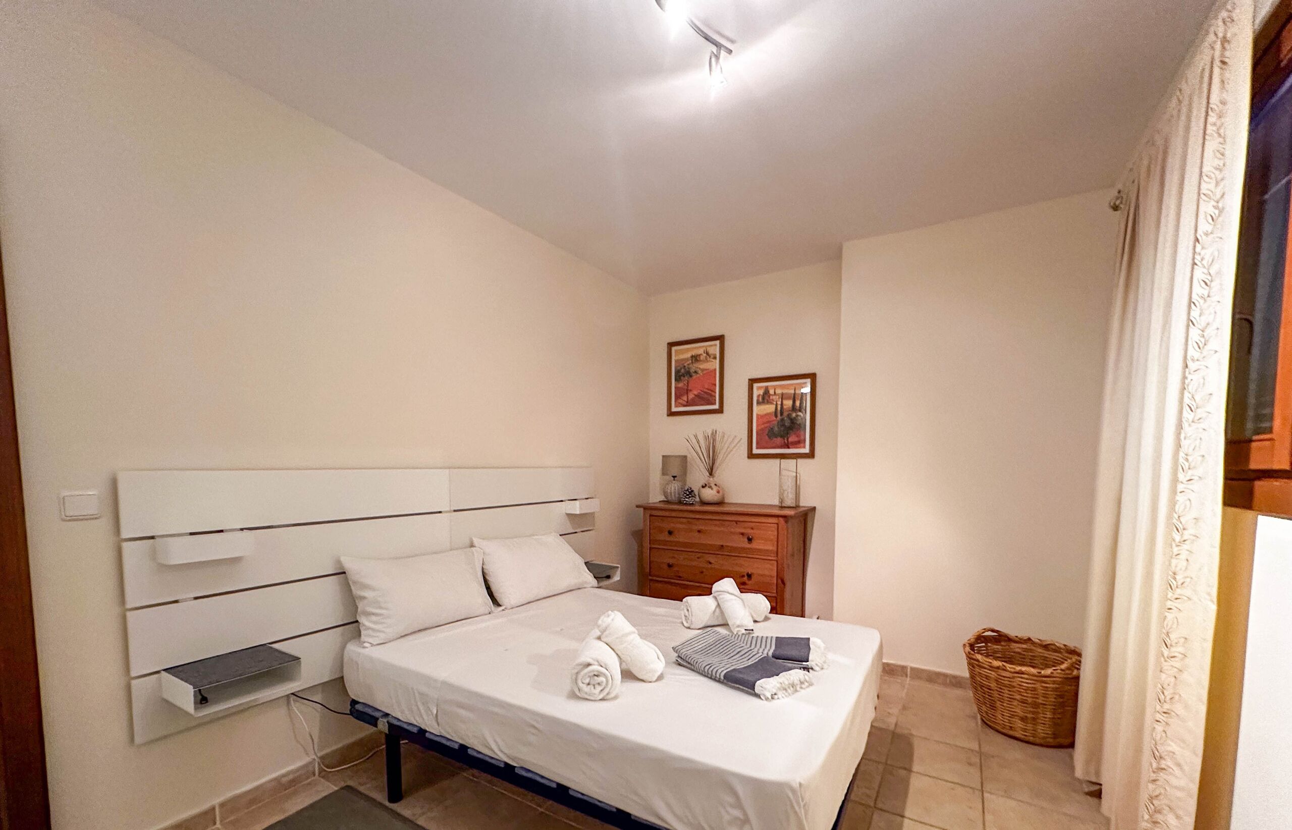 Een netjes opgemaakt slaapkamer met een bed, nachtkastjes, een dressoir en een wandplank.