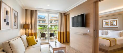 Habitación de hotel con sofá, mesa de centro, televisor, cama y balcón con vistas a edificios.