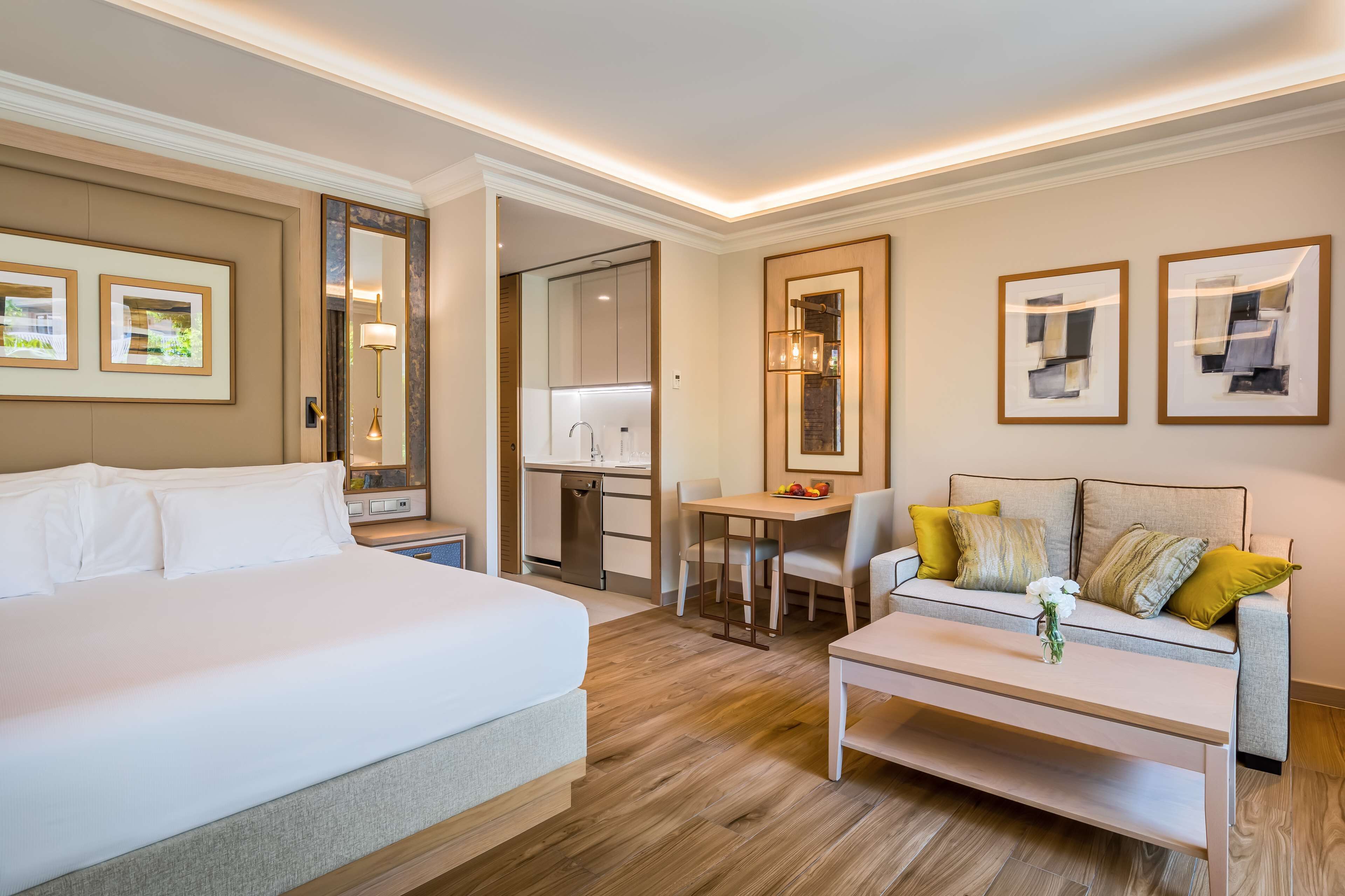 A hotel room with a large bed, a sofa, a dining table, and a kitchen area.