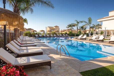 Una piscina al aire libre, sombrillas, sillones reclinables de piscina