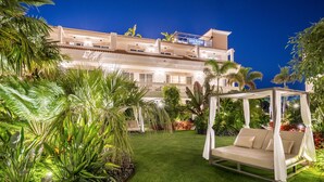 A well-maintained garden with a swing chair, lush greenery, and a building with a balcony in the background. - Barcelo La Nucía Hills (La Nucia)