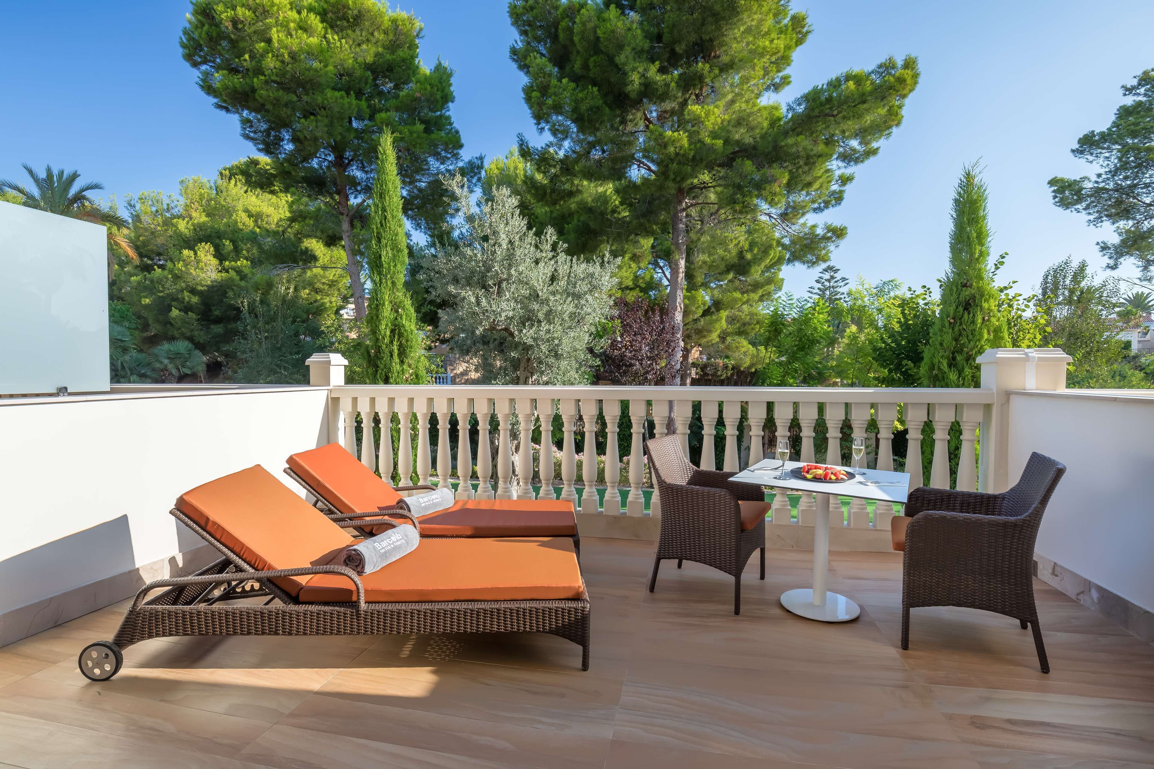 Un balcone con poltrone in vimini, un tavolo e vista sugli alberi.