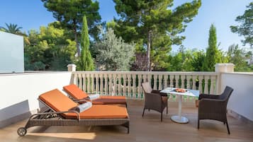 Un balcón con sillones de mimbre, una mesa y vistas a árboles.
