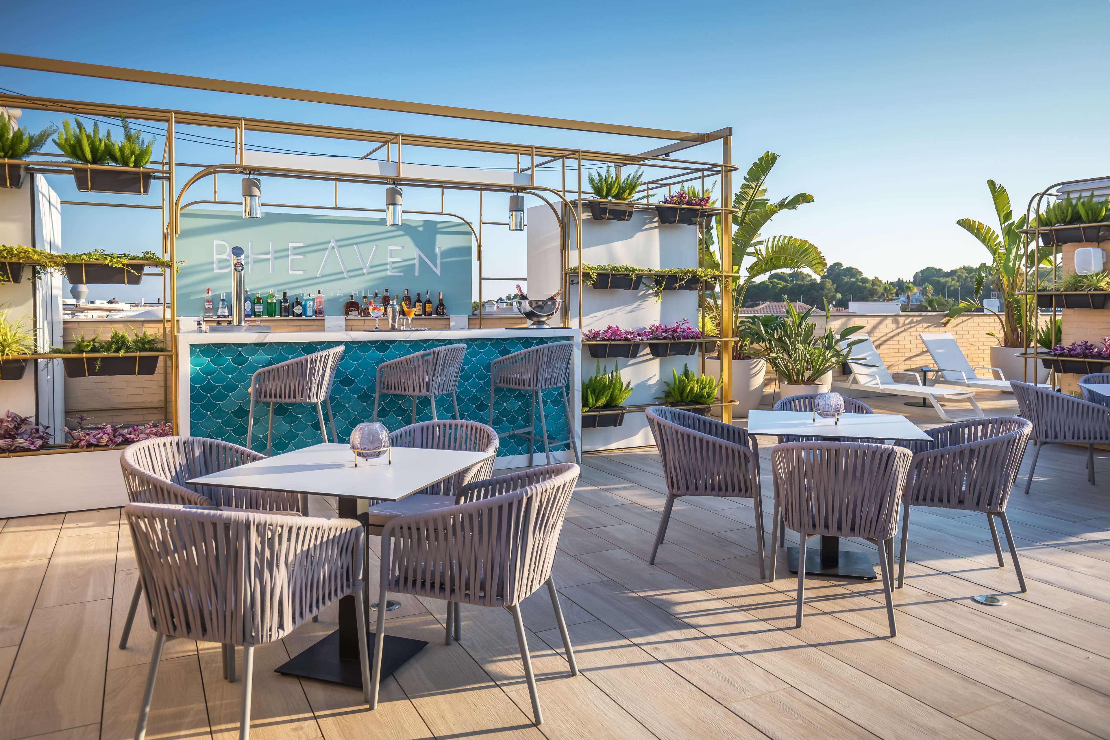 An outdoor patio with tables and chairs, a bar area with a blue-tiled backsplash, and potted plants.