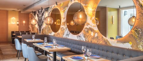 A restaurant with round mirrors, wooden tables, and grey upholstered seating.