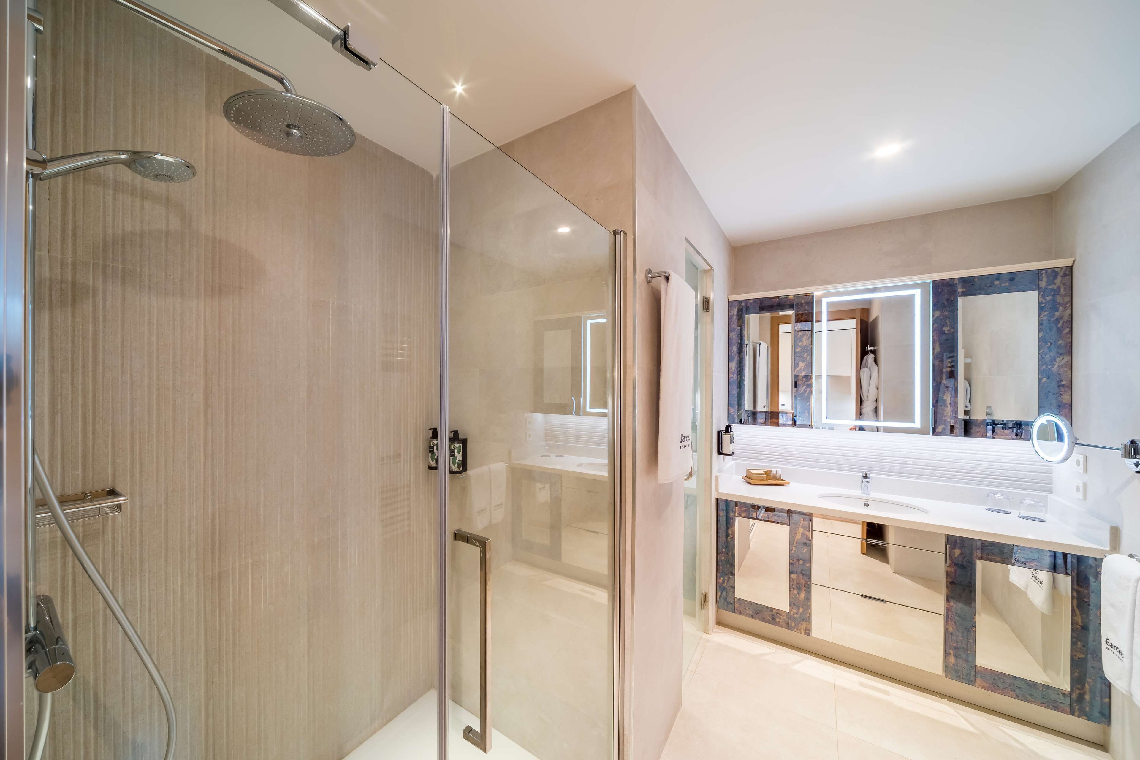 A modern bathroom with a glass shower enclosure, a large mirror, and a vanity with a marble countertop.