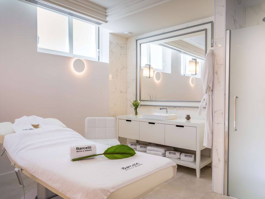 Un baño moderno con un tocador blanco, un espejo grande y una cama con bata y toalla blancos.