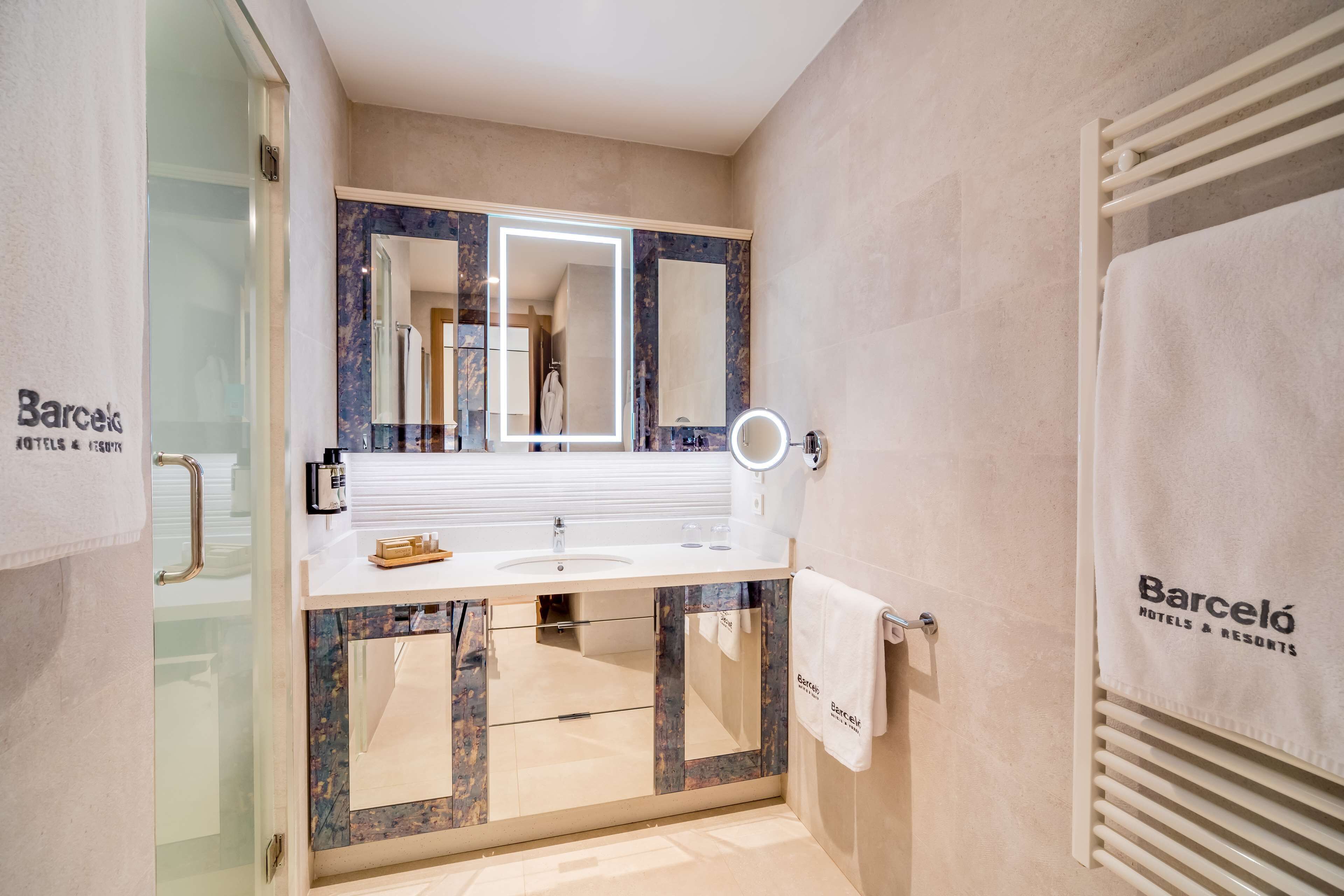 A modern bathroom with a white sink, a large mirror with built-in lighting, and a towel rack with a towel hanging on it.