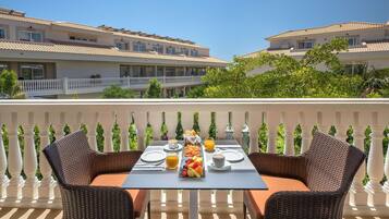 A dining table set with breakfast items on a balcony with white balustrades and a view of hotel buildings.