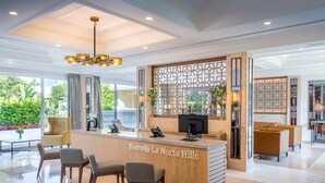 A hotel reception area with a modern design, featuring a reception desk, seating area, and large windows offering a view of the outdoors. - Barcelo La Nucía Hills (La Nucia)