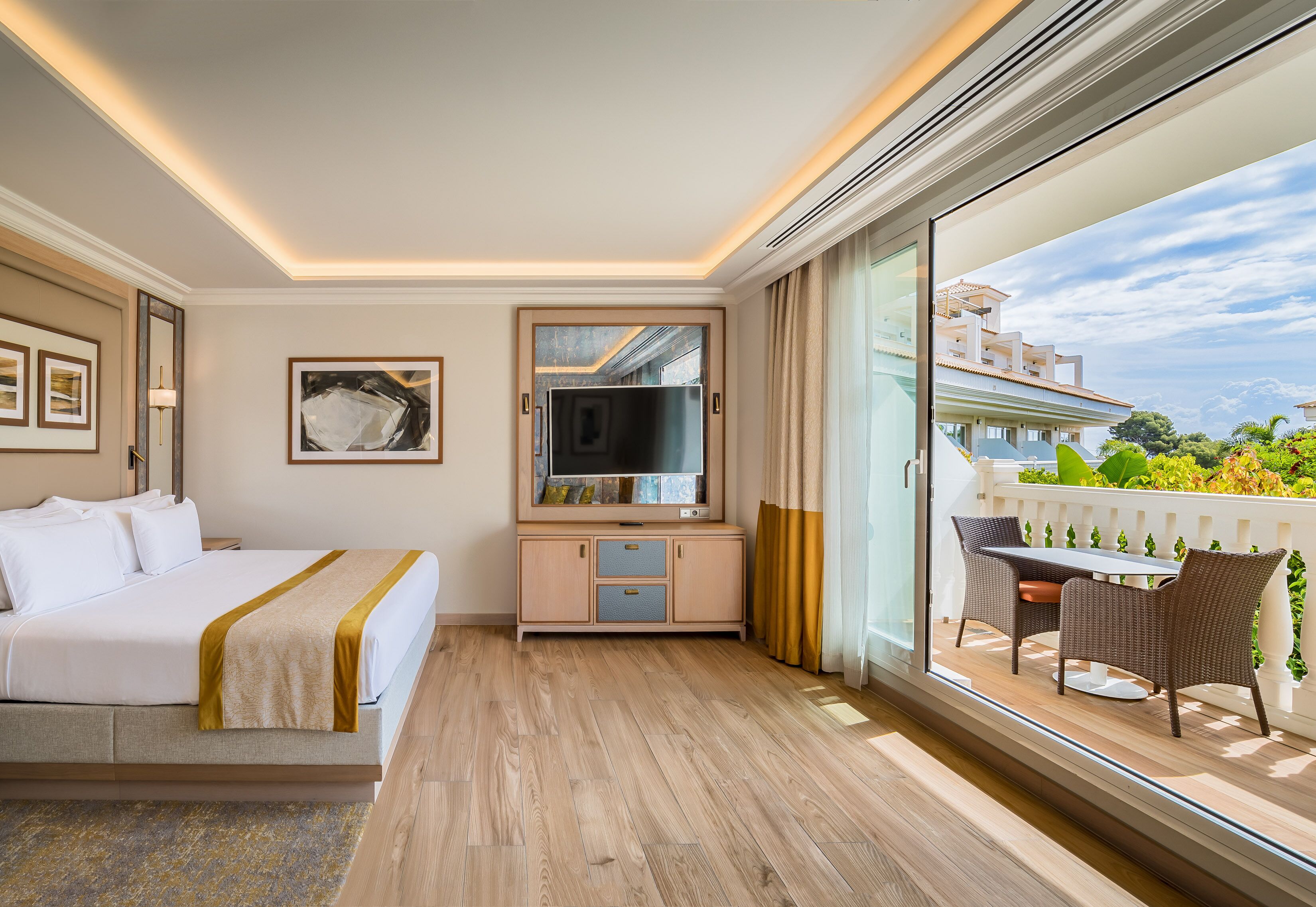 Habitación de hotel con cama, televisor, balcón con mesa y sillas, y vistas al exterior.