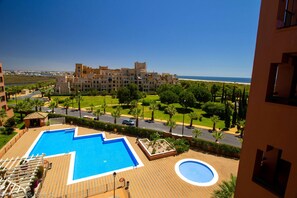 Relax by the large rectangular and circular pools in a serene, seaside setting surrounded by lush greenery and palm trees.