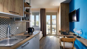 A modern kitchen with a wooden countertop, a sink, and a kettle. There is a dining area with a chair and a table, and a TV mounted on the wall. - Theasea Stylish Residences (Mylopotamos)