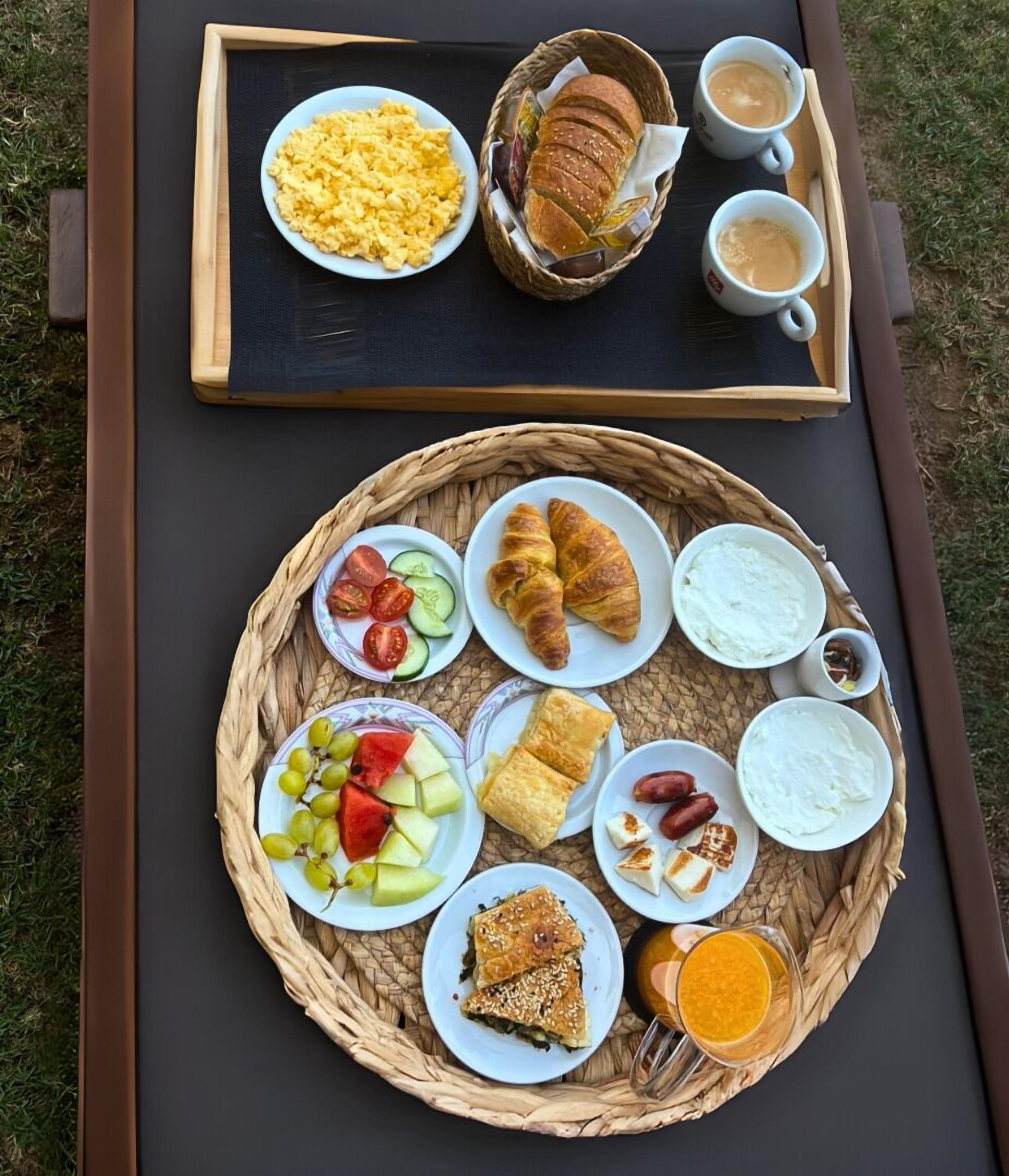 Bandeja de desayuno con huevos revueltos, cruasanes y café sobre una mesa al aire libre.