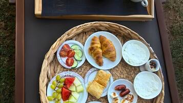 Bandeja de desayuno con huevos revueltos, cruasanes y café sobre una mesa al aire libre.