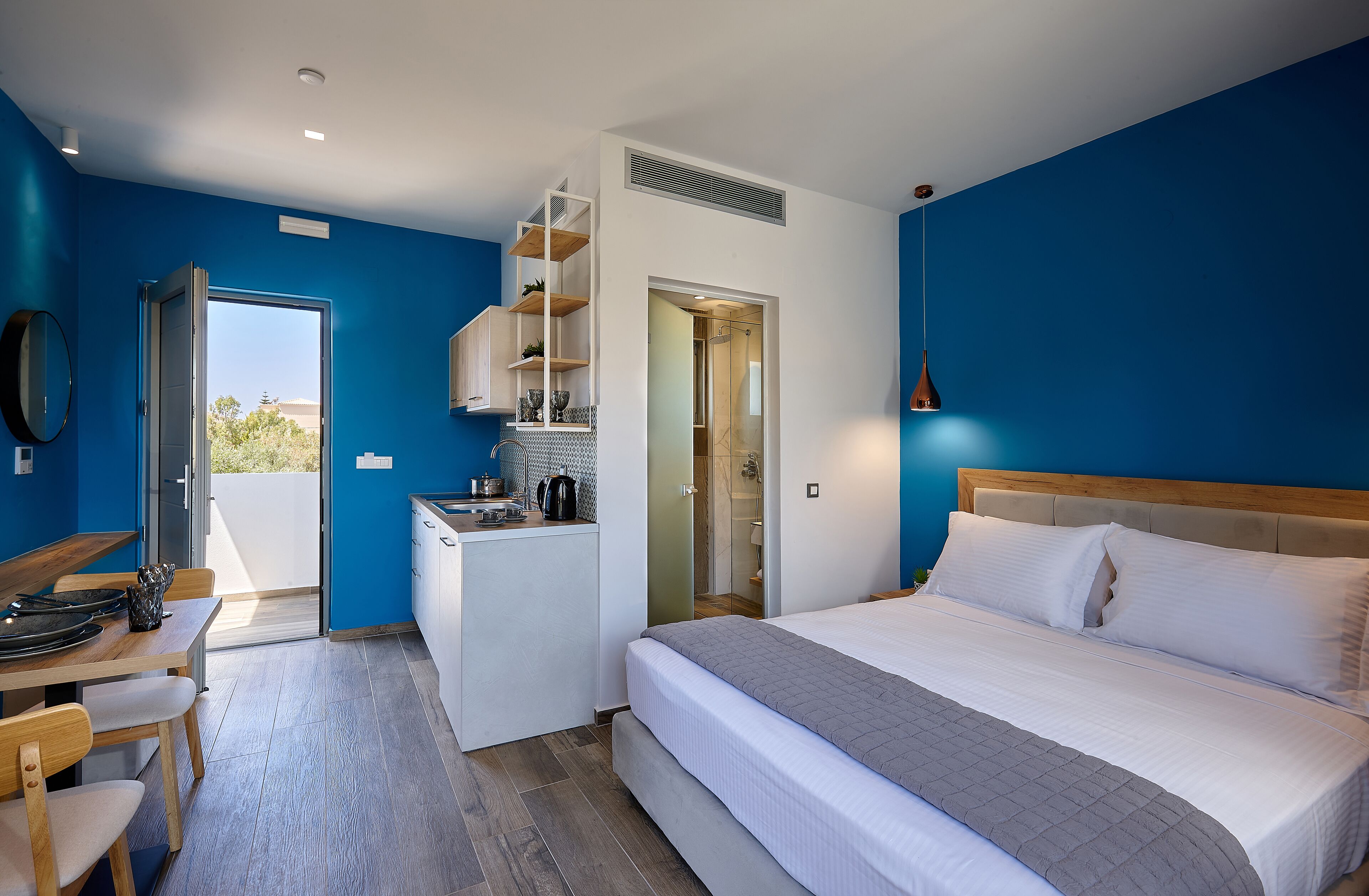 Habitación de hotel compacta con cama, kitchenette pequeño, zona de comedor y ducha.