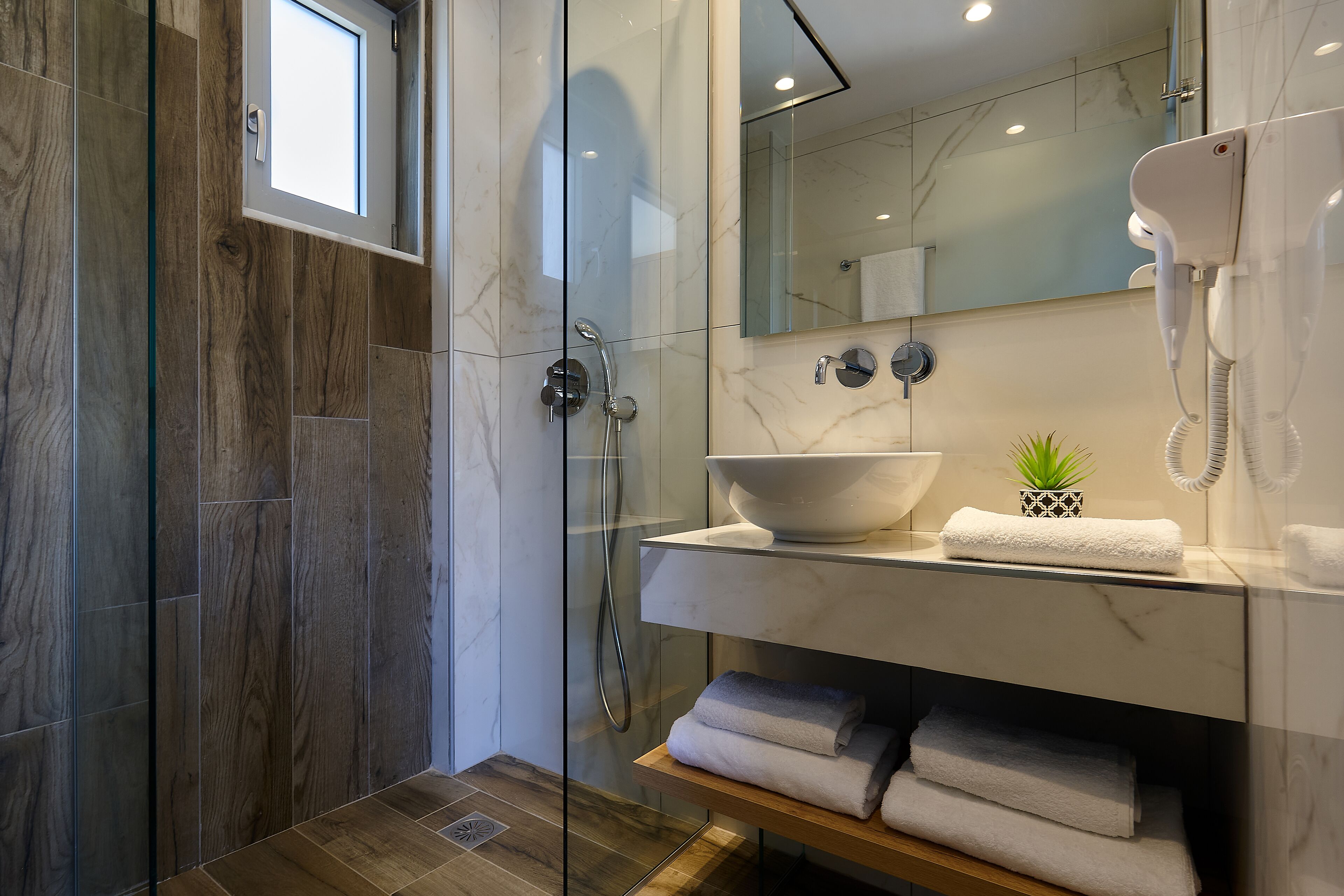 A modern bathroom with a glass-enclosed shower, a marble sink, and a built-in phone.