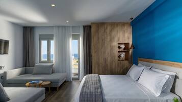 Quarto de hotel moderno com uma cama, um sofá, uma mesinha e vista para o exterior.