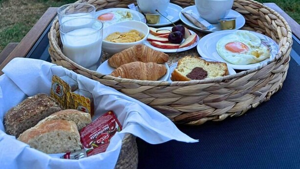 A breakfast tray with croissants, bread, eggs, and fruit by a poolside with stone walls and greenery in the background. - Theasea Stylish Residences (Mylopotamos)