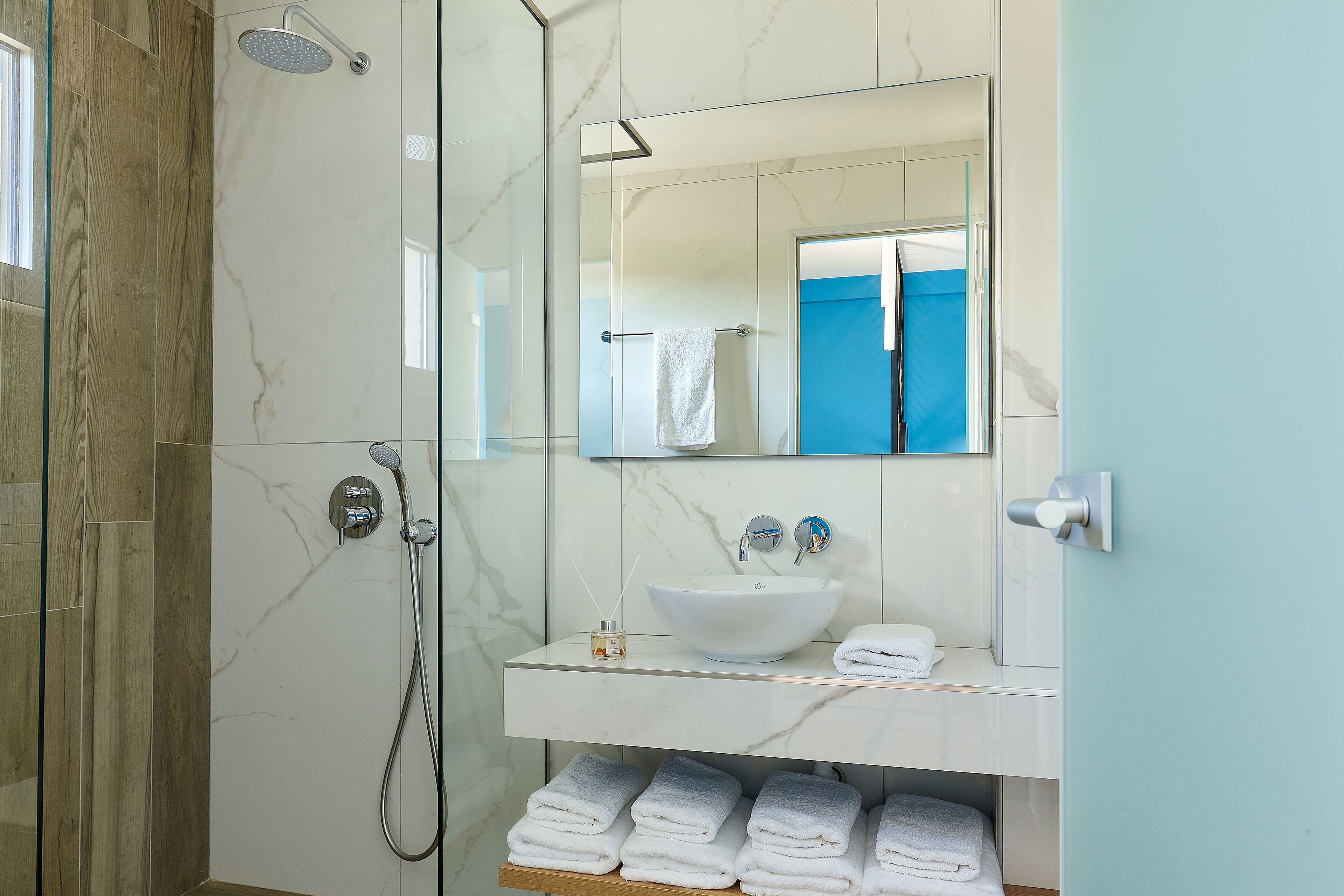 Un baño moderno con cabina de ducha de vidrio, un lavabo de mármol y un espejo sobre el mueble.