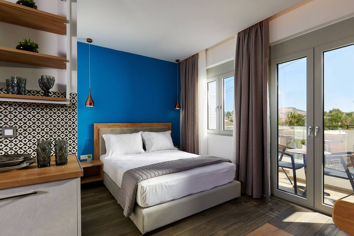 A modern bedroom with a large bed, a wooden bedside table, and a view of the outdoors through a sliding glass door.