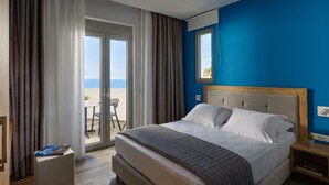 A hotel room with a bed, a nightstand, a window, and a view of the sea. - Theasea Stylish Residences (Mylopotamos)