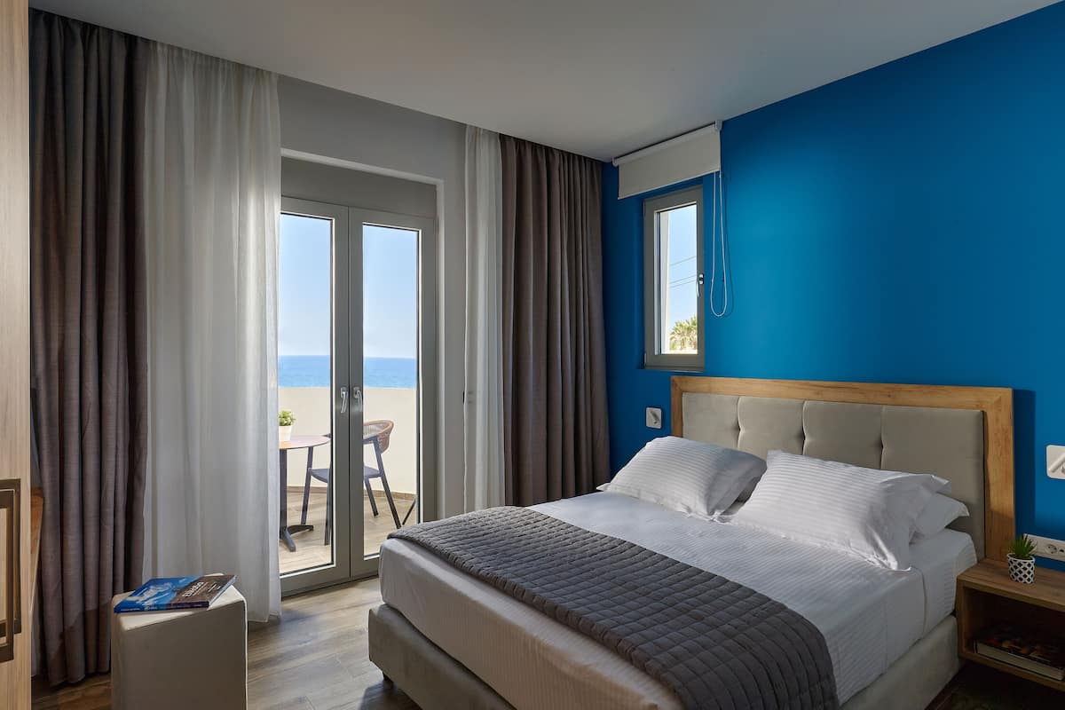 A hotel room with a bed, a nightstand, a window, and a view of the sea.