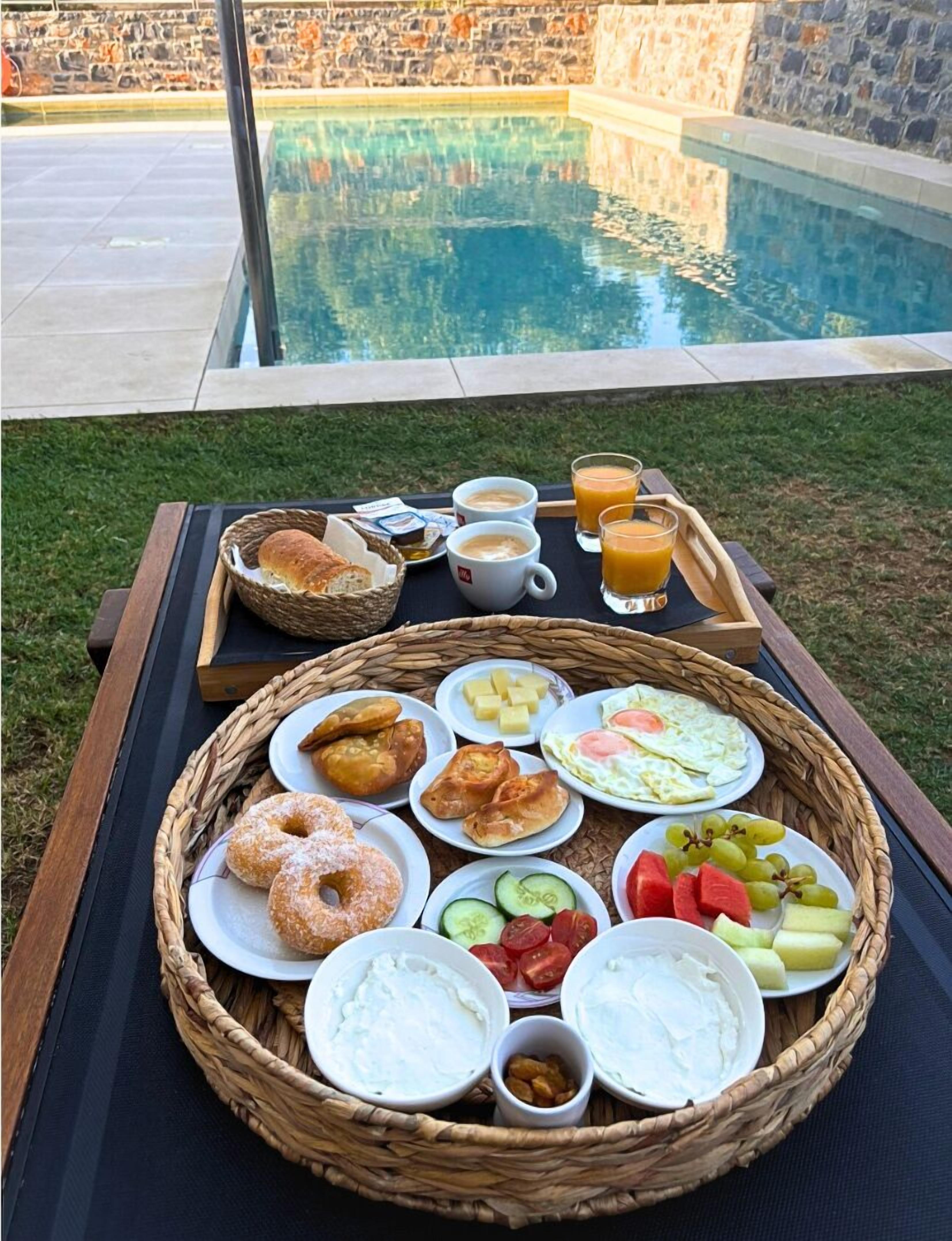 A breakfast tray with pastries, fruits, and beverages by a poolside.