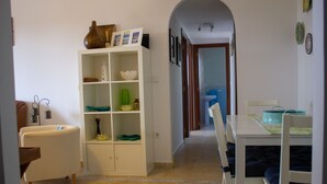 Un coin repas avec une table et des chaises blanches, un meuble blanc agrémenté d’objets décoratifs et un sol carrelé.