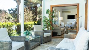 A sunlit room with wicker furniture, a glass table, and a view of a garden. - Luxurious Villa "Las Hortensias" with Private Pool, Garden & Wi-Fi (Santa Brígida)