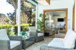 A sunlit room with wicker furniture, a glass table, and a view of a garden.