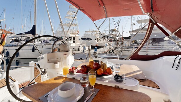 Una mesa de desayuno con alimentos, en un barco rodeado de otros barcos.