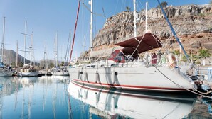 Un puerto deportivo con barcos amarrados, agua tranquila y un acantilado rocoso al fondo.