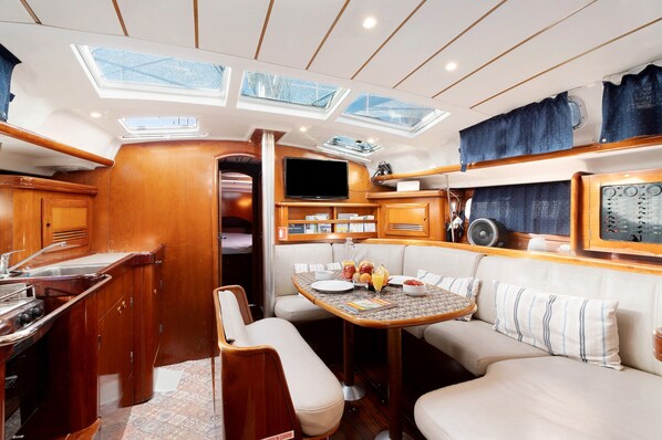 A compact galley with a sink, stove, and a flat-screen TV. There are cushioned seating areas and a small table with a fruit bowl.