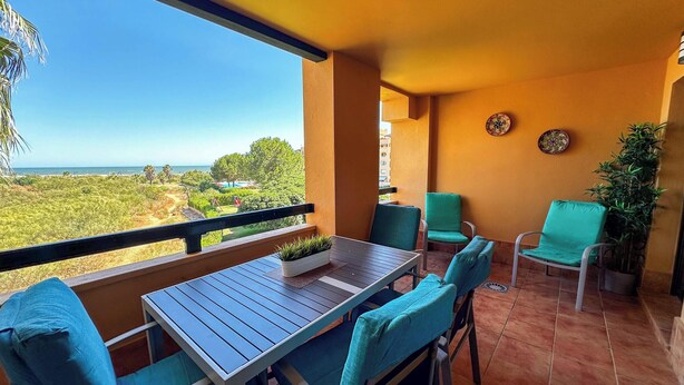Een balkon met een tafel en stoelen, uitzicht op zee en een plant in een pot.