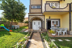 Une maison à deux étages avec une entrée à l’avant, un balcon et un patio aménagé avec du mobilier d’extérieur.