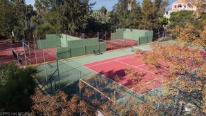 Una cancha de tenis rodeada de árboles y un edificio al fondo.