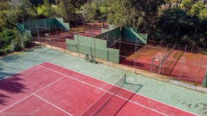 Un campo da tennis con superfici verdi e rosse, circondato da alberi e una recinzione.