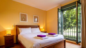 Habitación de hotel con una cama grande, dos mesitas de noche con lámparas y vistas a un jardín a través de un ventanal corredero.