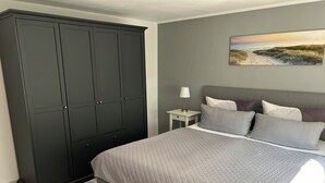 A bedroom with a large dark wardrobe, a bed with multiple pillows, a nightstand with a lamp, and a painting on the wall. - Ferienwohnung Weidenblick (Barth)