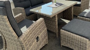 A sunroom with wicker furniture, a glass table, and a view of a grassy field. - Ferienwohnung Weidenblick (Barth)