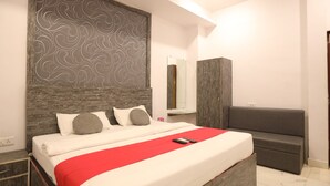 A modern bedroom with a bed, a bedside table, a mirror, and a grey sofa. - Hotel Gaurishree (Bhopal)