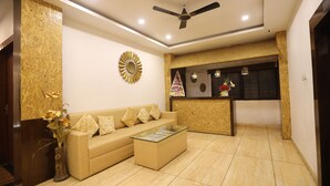A modern living room with a beige sofa, a glass coffee table, and a decorative mirror on the wall. - Hotel Gaurishree (Bhopal)