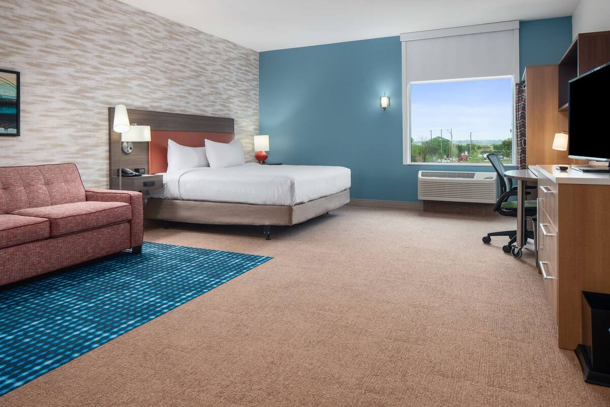 A hotel room with a bed, a desk, a chair, a sofa, and a large window.