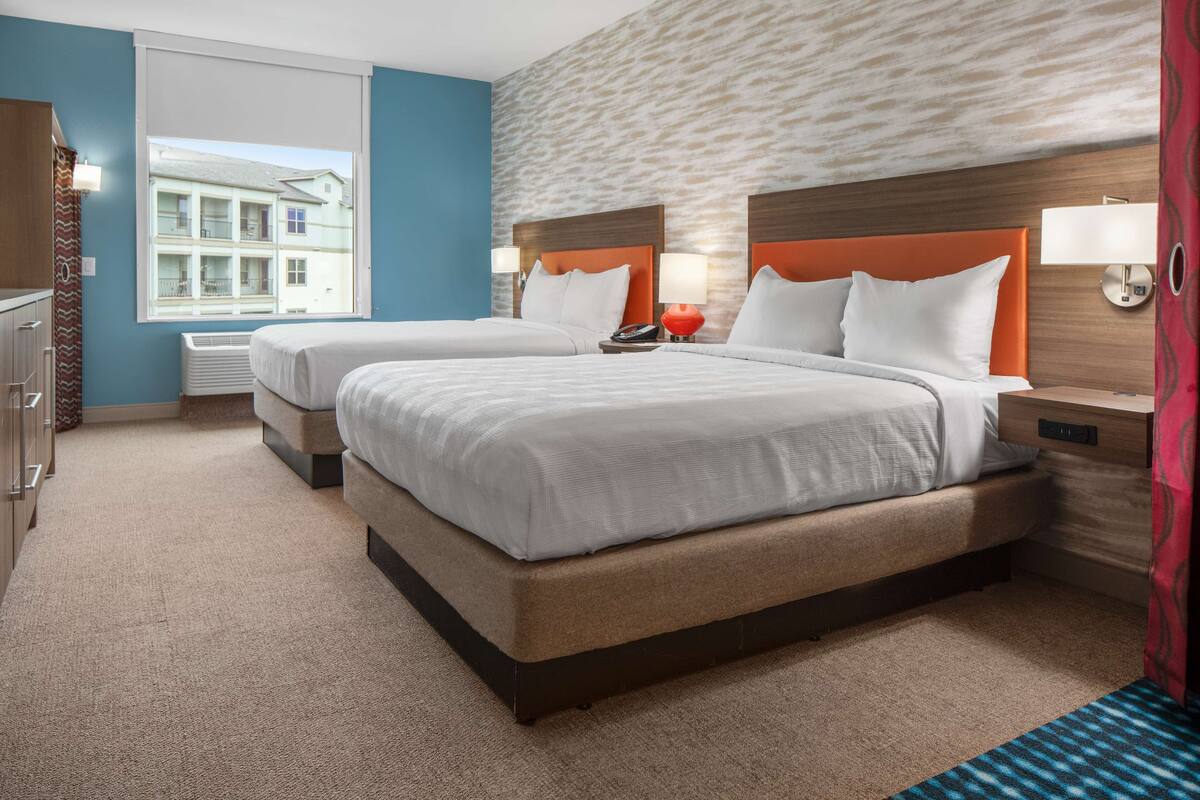 A hotel room with two beds, a large window, and a view of a building outside.