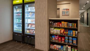 Un couloir d’hôtel avec deux distributeurs de boissons réfrigérés, l’un portant l’étiquette « froid » et l’autre « très froid », ainsi qu’une étagère remplie de collations et de boissons.