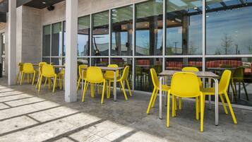 A modern indoor dining area with yellow chairs and tables, large windows, and a view of the outside.