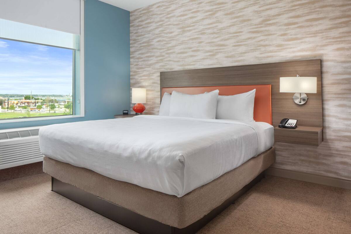 A hotel room with a large bed, a view of the city, and a modern design.