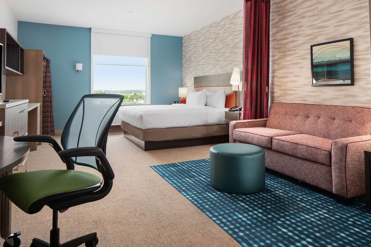 A hotel room with a bed, a sofa, a desk, and a chair.