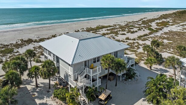 A beachfront property with a large house featuring multiple balconies, a covered patio, and a view of the ocean.